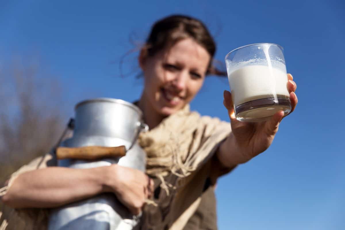 hübsche Bäuerin präsentiert frische Milch von der Kuh